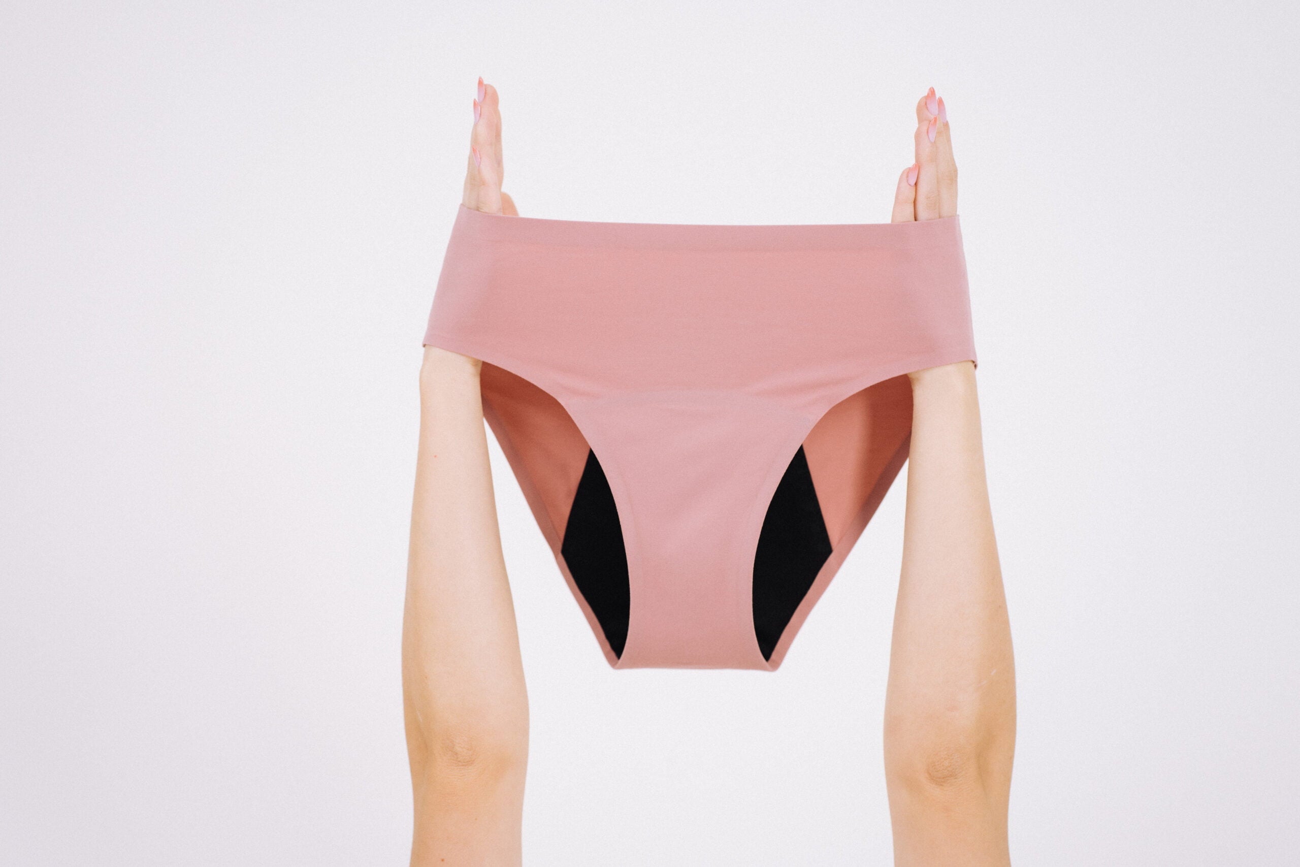 Chilot menstrual roz prăfuit, ținut în mâini ridicate, evidențiind designul seamless și stratul absorbant interior.