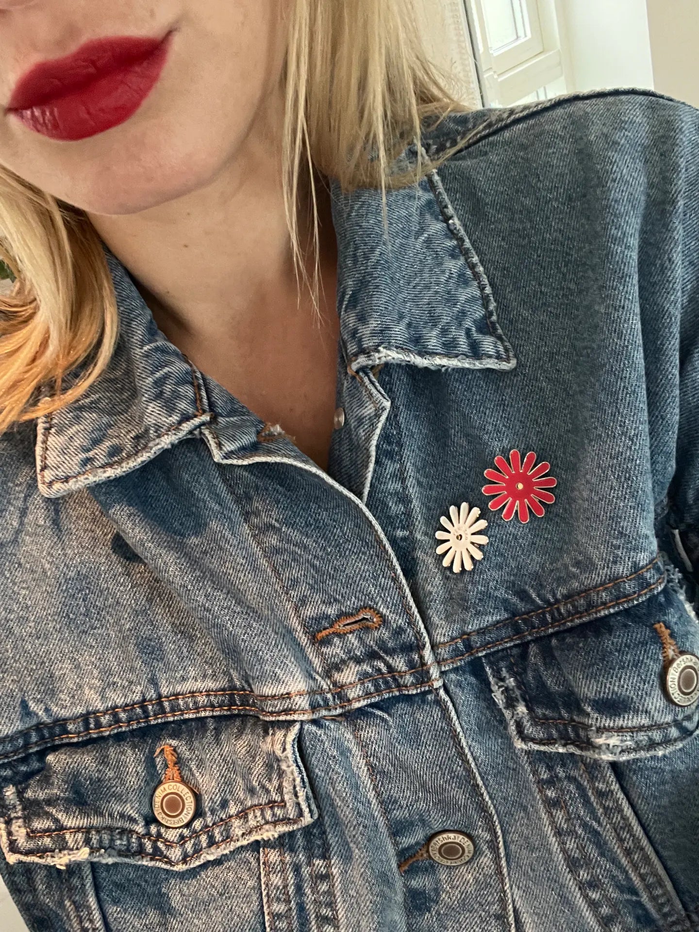 Femeie purtând geacă de blugi decorată cu insigne în formă de floare Femi.Eko®, una albă și una roșie, simbol al feminității și solidarității.